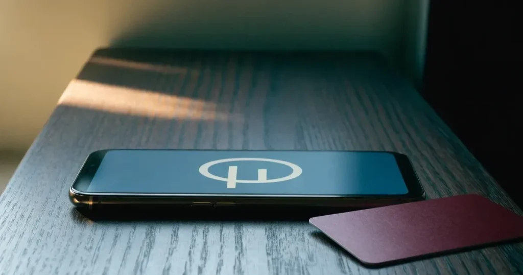 Uno smartphone e una carta di pagamento affiancati su un tavolo di legno, con alcune banconote da euro accanto